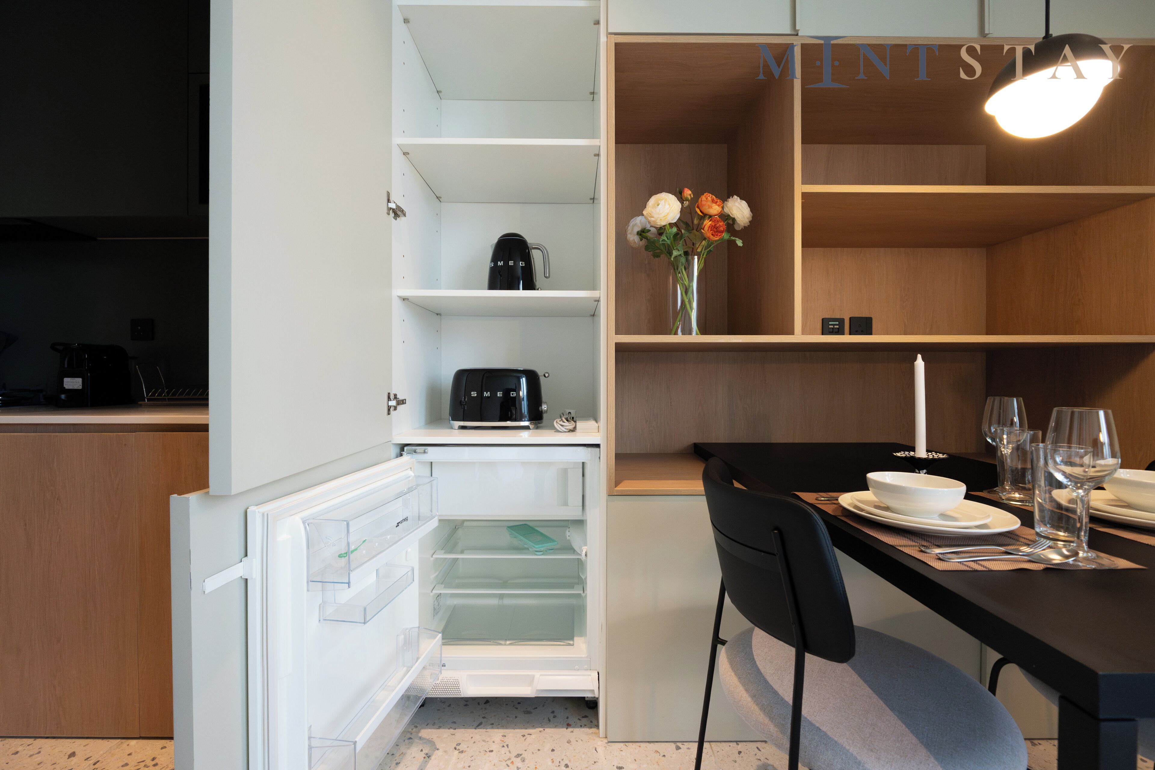 Eine moderne Küche mit einem integrierten Kühlschrank, einer Kaffeemaschine und einem Essbereich mit Tisch für zwei Personen.