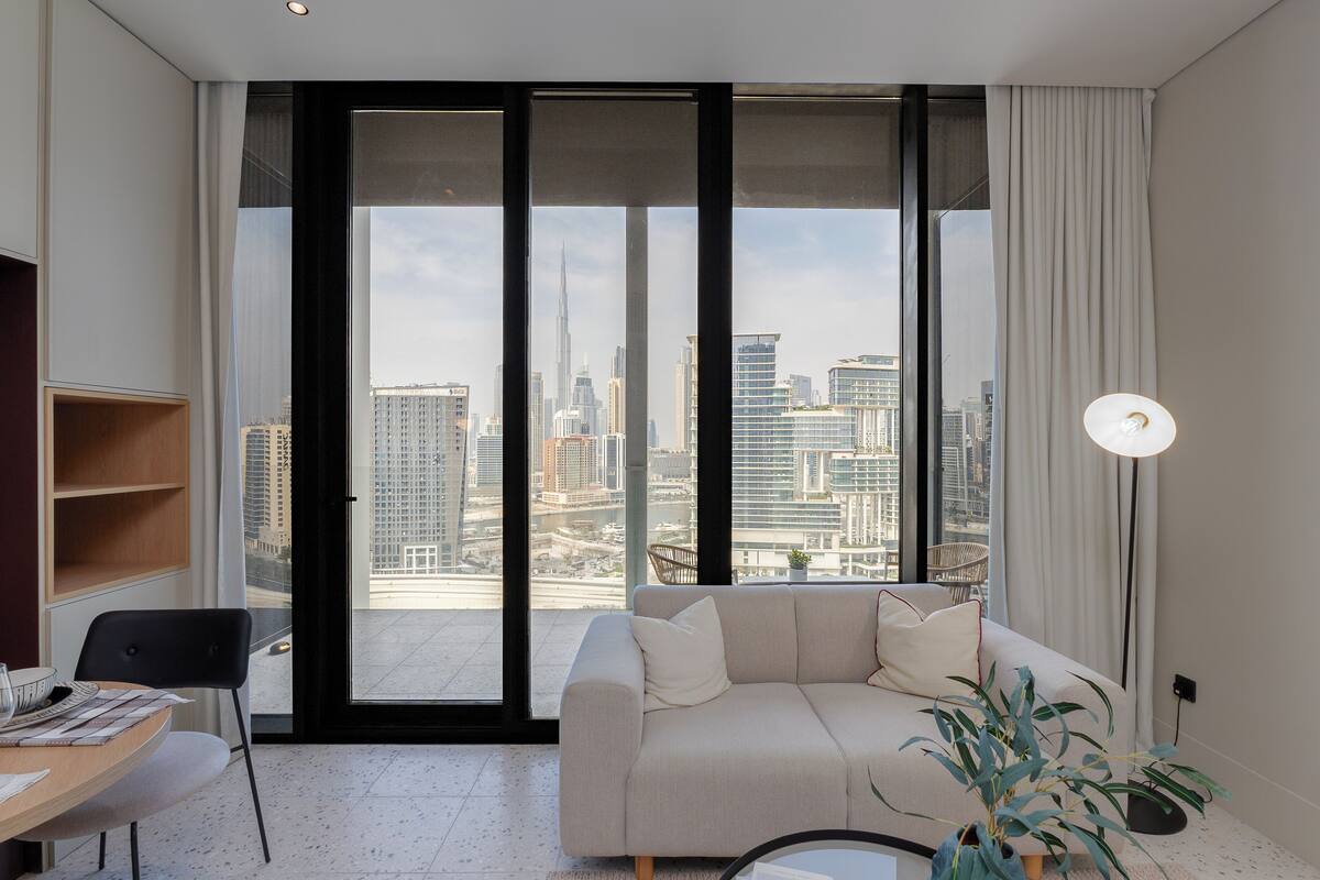 A modern living room with a large window, a sofa, a dining table, and a plant.