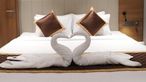 A hotel room with a neatly made bed, two pillows, and a decorative swan design on the bedspread. - Hotel Grand Alleppey (Ambalapuzha)