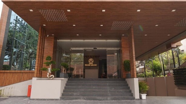 A hotel entrance with a modern design, featuring a wooden facade, a staircase leading to the entrance, and potted plants. - Hotel Grand Alleppey (Ambalapuzha)