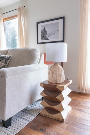 A living room with a sofa, a wooden side table with a lamp, a framed picture on the wall, and a window with curtains. - Romantic Swiss Chalet with Mountain Views (Golden)