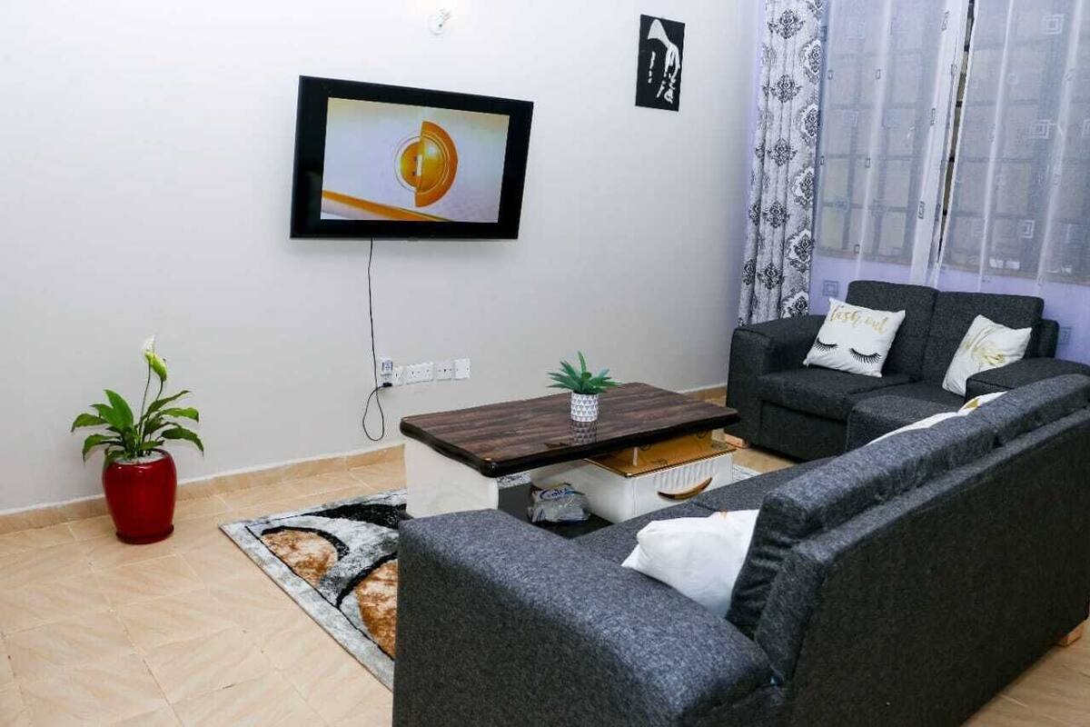 A living room with a TV mounted on the wall, a sofa set, a coffee table, and a potted plant.