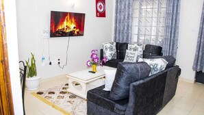 Ein Wohnzimmer mit Sofa, Couchtisch, Kamin, Blumentopf und einem Fenster mit Vorhängen.