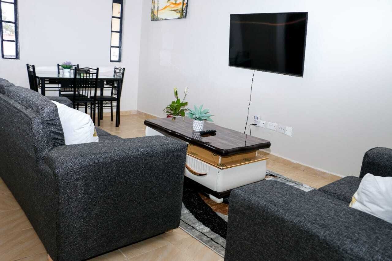 A modern living room with grey sofas, a coffee table, and a flat-screen TV mounted on the wall.