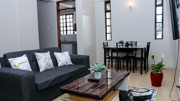 Ein Wohnzimmer mit grauem Sofa, einem Holztisch, einem Esstisch mit Stühlen und einem roten Topf mit Pflanze.