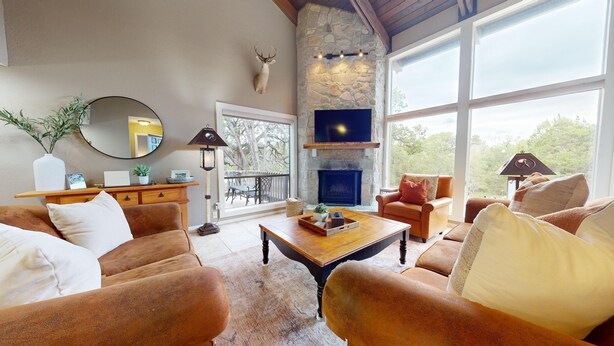 A cozy living room with leather sofas, a fireplace, and a stone wall. - River City Resorts: TBM 121: Spacious Hill Country Condo at T Bar M Ranch (New Braunfels)