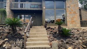 A two-story house with a stone facade, large windows, and a wooden balcony. - River City Resorts: TBM 121: Spacious Hill Country Condo at T Bar M Ranch (New Braunfels)