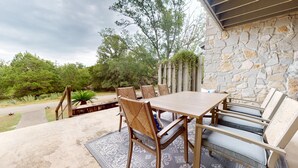 An outdoor patio with a stone wall, a wooden table, and wicker chairs. - River City Resorts: TBM 121: Spacious Hill Country Condo at T Bar M Ranch (New Braunfels)