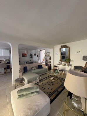 A living room with a sofa, ottoman, coffee table, and a lamp. There is a bookshelf and a mirror on the wall. - Ground-floor apartment, terrace, a 15-minute walk from downtown Arles (Arles)