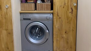 A compact laundry room with a front-loading washing machine, wooden cabinets, and storage boxes.