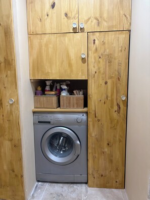 Une petite buanderie équipée d’un lave-linge à chargement frontal, de meubles en bois et de boîtes de rangement.