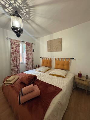 A bedroom with a bed, a nightstand, a lamp, and a window with curtains.