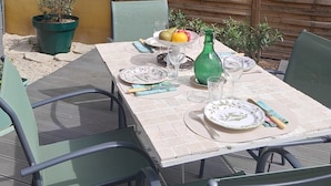 An outdoor dining area with a table set for four, surrounded by chairs, against a yellow wall with a wooden fence.