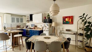 A modern kitchen with a dining area, featuring a central island, pendant lighting, and a view of the living room.
