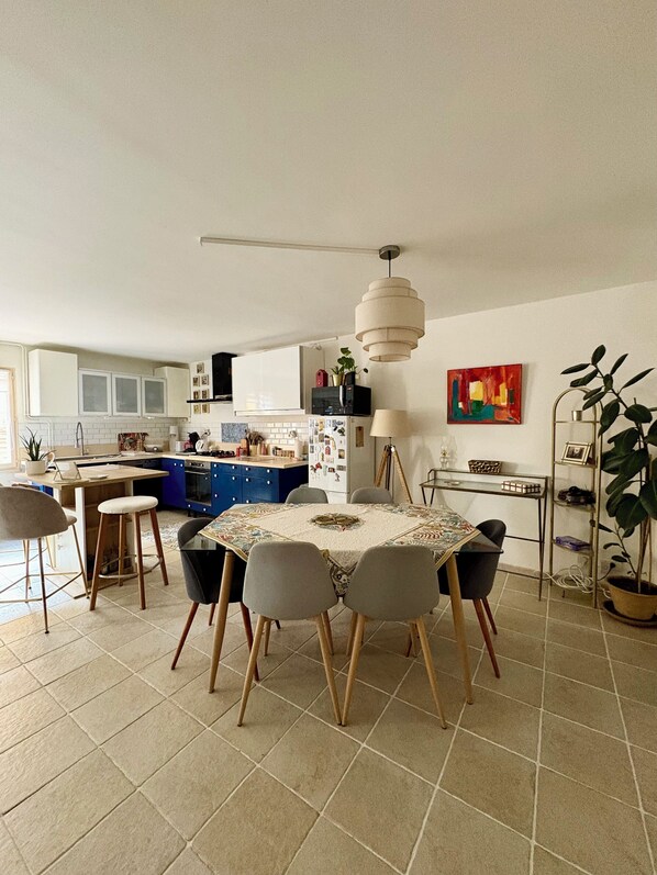 A modern kitchen with a dining area, featuring a central island, pendant lighting, and a view of the living room.