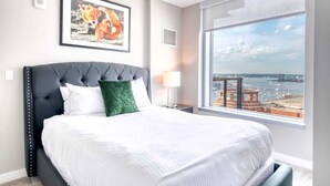 Ein modernes Hotelzimmer mit einem großen Bett, Blick auf die Stadt und einem gerahmten Kunstwerk darüber.
