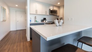 A modern kitchen with white cabinets, a stainless steel microwave, and a large island with bar stools. - Luxury Apt Near Charles River with Sky Terrace Access (Cambridge MA)