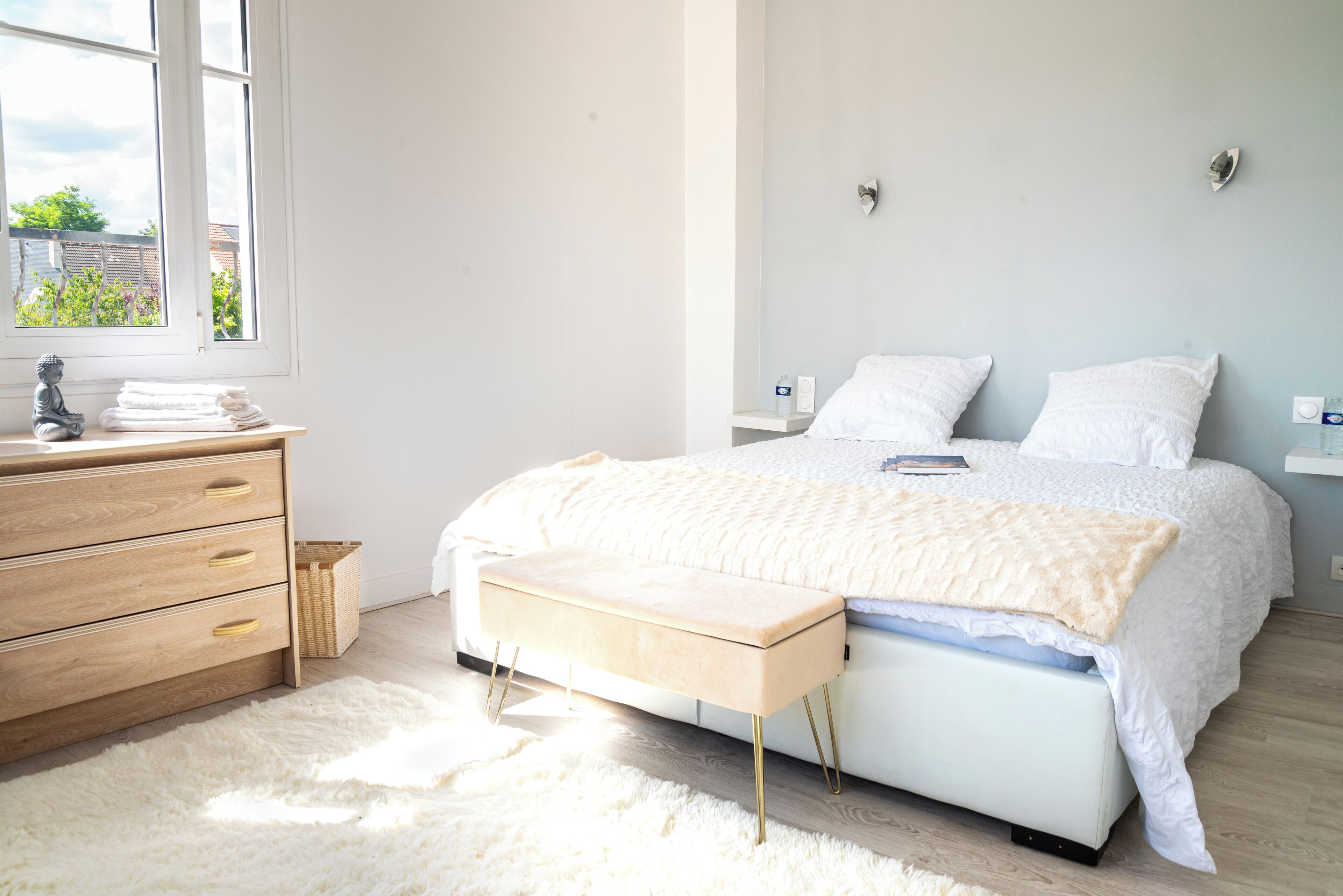 A bedroom with a bed, a wooden dresser, a bench, and a window.