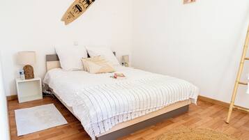 Een netjes opgemaakt slaapkamer met een bed, nachtkastjes, een bord aan de muur en een geweven mat op de vloer.