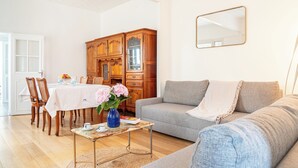 A living room with a dining area, a grey sofa, a wooden cabinet, and a mirror on the wall.