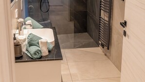 Een moderne badkamer met een douchecabine, een wit wastafelmeubel met toiletartikelen en een handdoekrek.