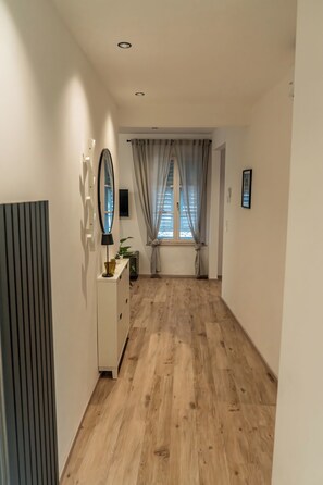 Een gang met houten vloer, een witte dressoir, een spiegel en een raam met gordijnen.