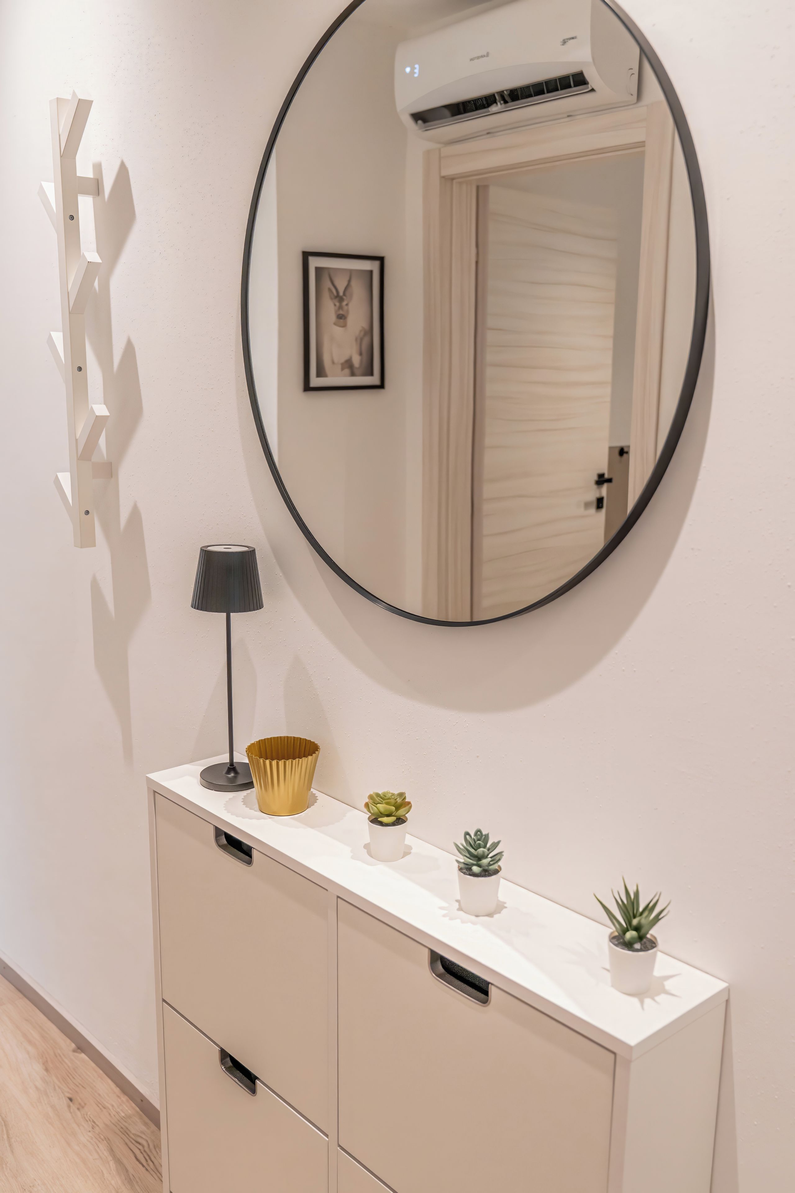Ein moderner Waschtisch mit rundem Spiegel, einer kleinen Lampe und Dekorationselementen, darunter eine goldene Schale und Topfpflanzen.