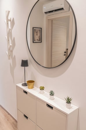 A modern bathroom vanity with a round mirror, a small lamp, and decorative items including a gold bowl and potted plants.