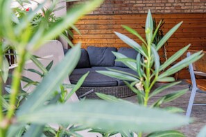 A wicker sofa with cushions against a brick wall, surrounded by greenery. - Centrally located vacation apartment in Tramin  (Tramin an der Weinstraße)