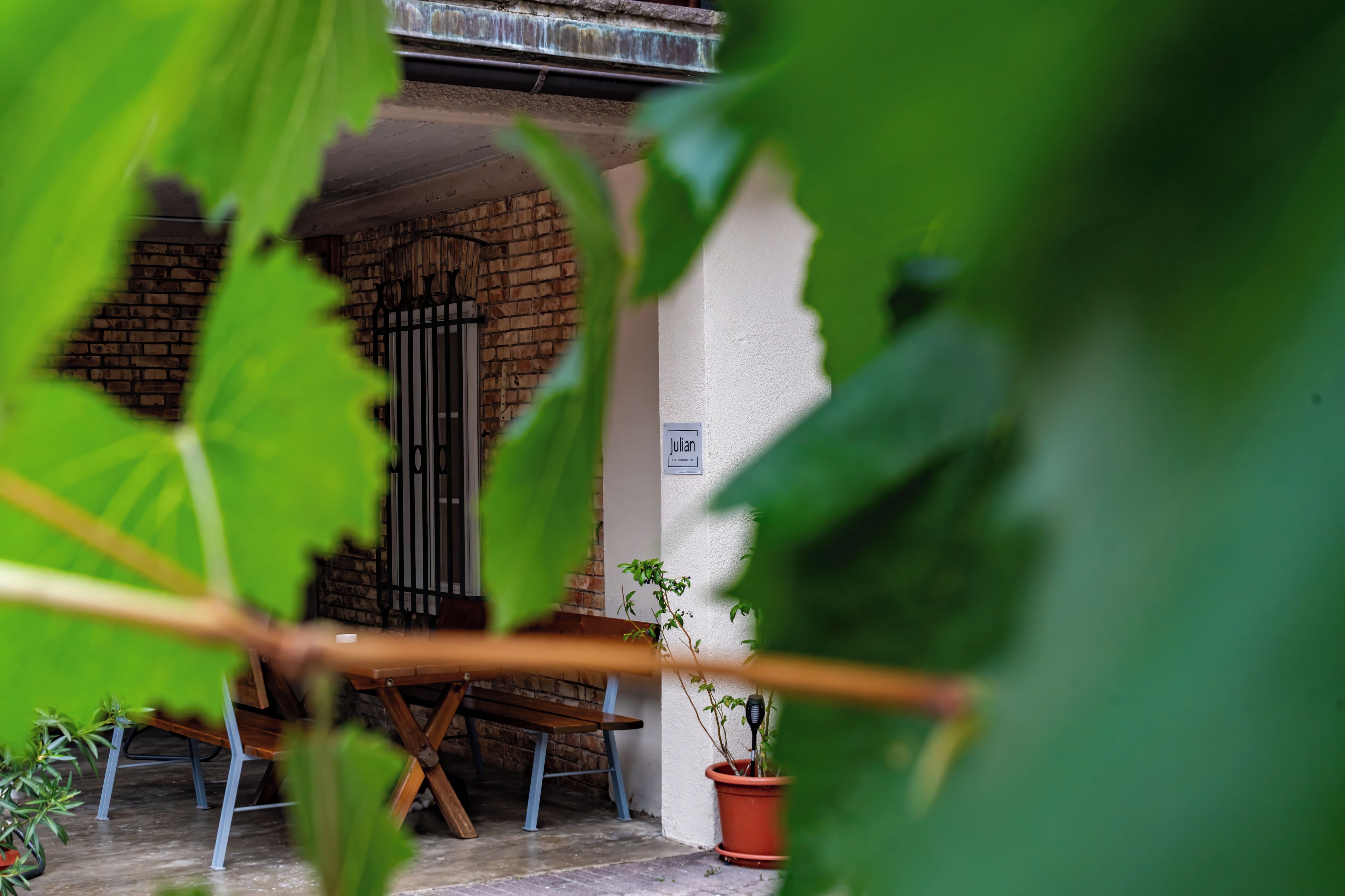 Una entrada de maó amb una reixa metàl·lica, una cadira de fusta i una planta en test.