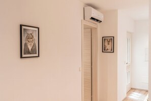 A hallway with framed pictures on the walls, a door with a wooden door frame, and an air conditioning unit mounted on the wall. - Centrally located vacation apartment in Tramin  (Tramin an der Weinstraße)