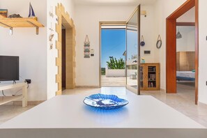 A modern living room with a large white table, a television on a stand, and a view of the outside through an open door. - 3954 Villetta Mamapace by Barbarhouse (Porto Cesareo)