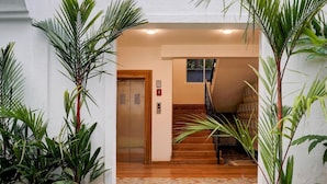 Entrada com piso de azulejos, plantas em vasos, elevador e escada.