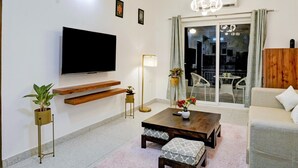 Uma sala de estar moderna com uma TV de tela plana, prateleiras de madeira, uma mesa de centro e um sofá.