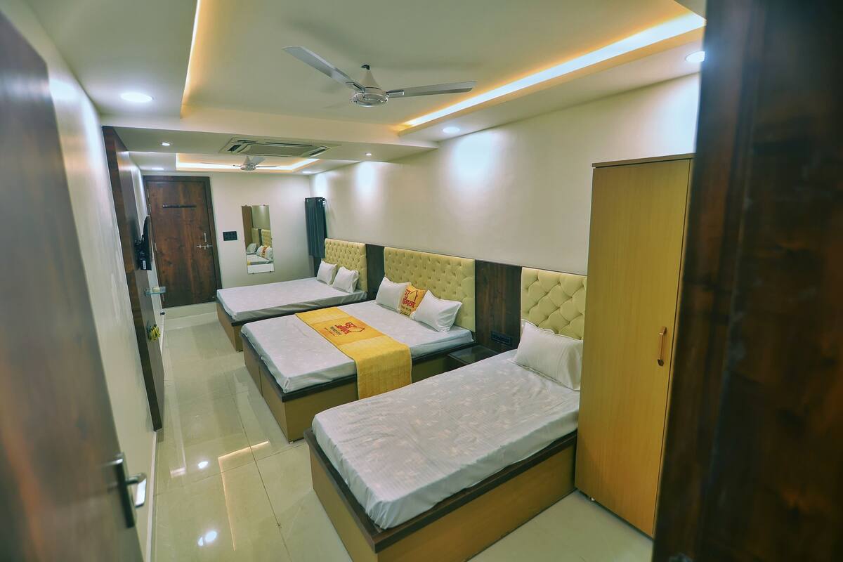 Quarto de hotel com duas camas, guarda-roupa, ventoinha no teto e iluminação embutida.