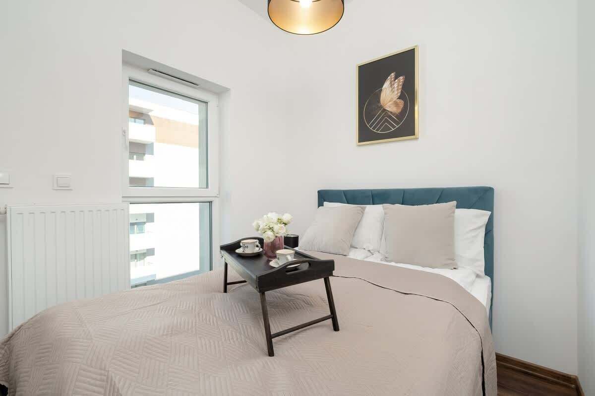 A bedroom with a bed, a bedside table with a tray, a window, and a wall-mounted picture.