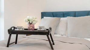 Un lit avec une tête de lit bleue, une table de chevet sur laquelle se trouve un plateau avec deux tasses et un vase de fleurs.