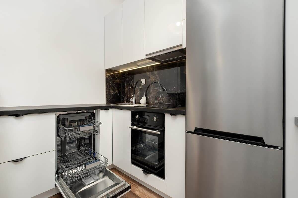 A modern kitchen with white cabinetry, a built-in dishwasher, a black oven, and a stainless steel refrigerator.