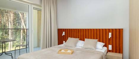 Una habitación de hotel con una cama grande, un cabecero de madera, una mesita de noche y un balcón con mesa y sillas.