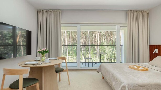 Ein Hotelzimmer mit Bett, einem Esstisch mit Stühlen, einem Fernseher und einem Balkon mit Tisch und Stühlen.