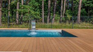 Ein Pool mit Wasserfall, umgeben von einer Holzterrasse und einem von Bäumen gesäumten, eingezäunten Bereich.
