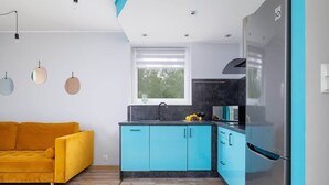 A modern kitchen with blue cabinets, a yellow sofa, and a stainless steel refrigerator. - Spacious Apartment | Parking, Balcony and Mountain View (Wisla)