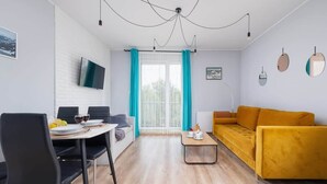 A modern living room with a sofa, dining table, chairs, and a TV. - Spacious Apartment | Parking, Balcony and Mountain View (Wisla)