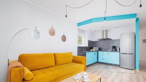 A modern living room with a sofa, a coffee table, and a kitchen area with cabinets and appliances. - Spacious Apartment | Parking, Balcony and Mountain View (Wisla)