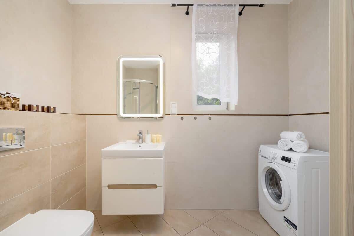 A bathroom with a toilet, sink, mirror, window, and washing machine.