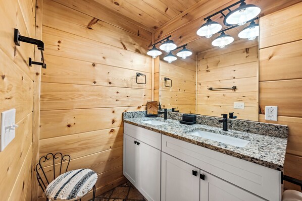 Un baño de estilo cabaña de madera con lavamanos de encimera de granito, un espejo y una lámpara en el techo.