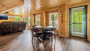 Ein Holzblockbau-Innenraum mit einem Esstisch und Stühlen, einem Sofa und einem großen Fenster mit Jalousien.