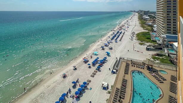 A beach resort with a long sandy beach, a swimming pool, and a high-rise hotel building.