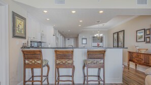 A kitchen with wooden bar stools, white cabinets, and a central island.