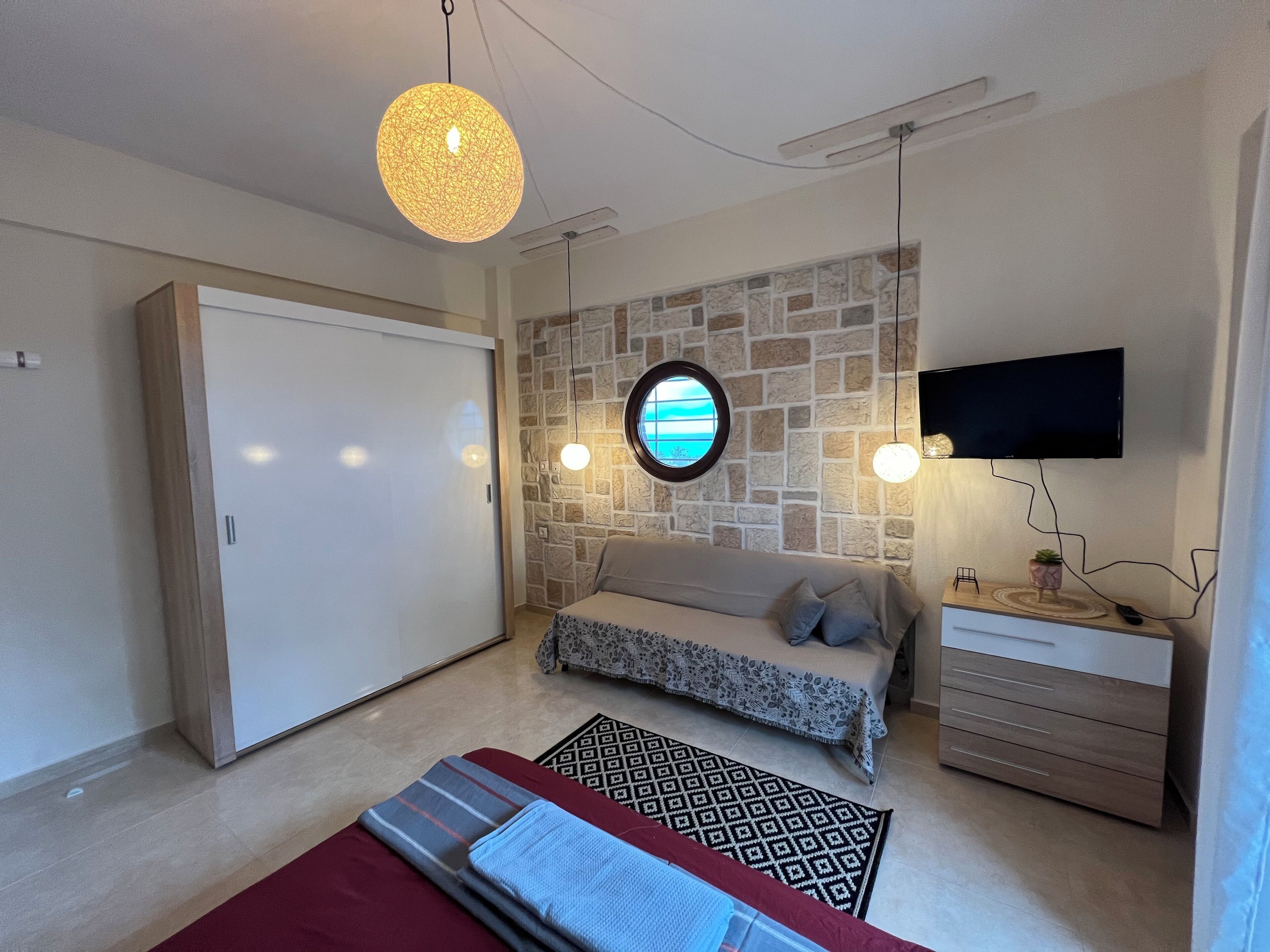 A bedroom with a bed, a TV mounted on the wall, a wardrobe, and a round light fixture.